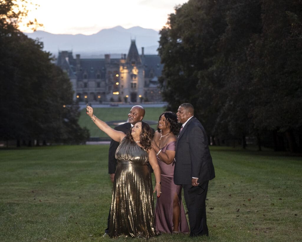 Wedding guests taking selfies during sunset with Biltmore Estate light up in the background