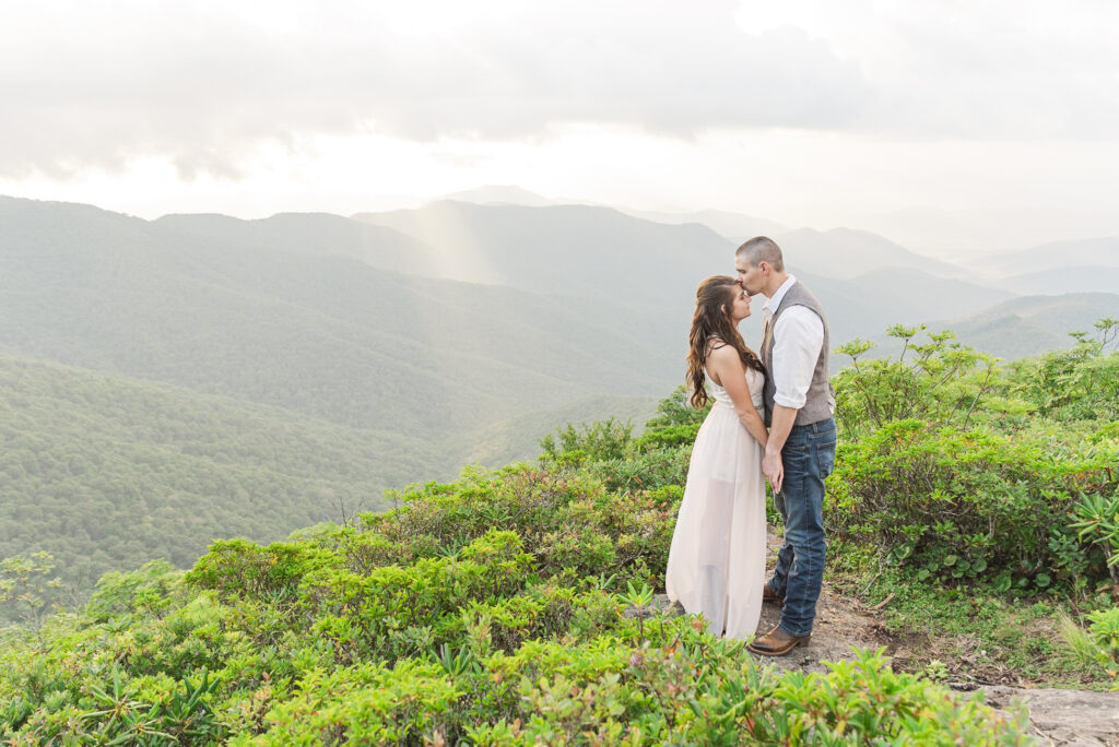 couple embracing at the top of craggy pinnacle on a cloudy spring day with a long view of the blue ridge parkway in the background
