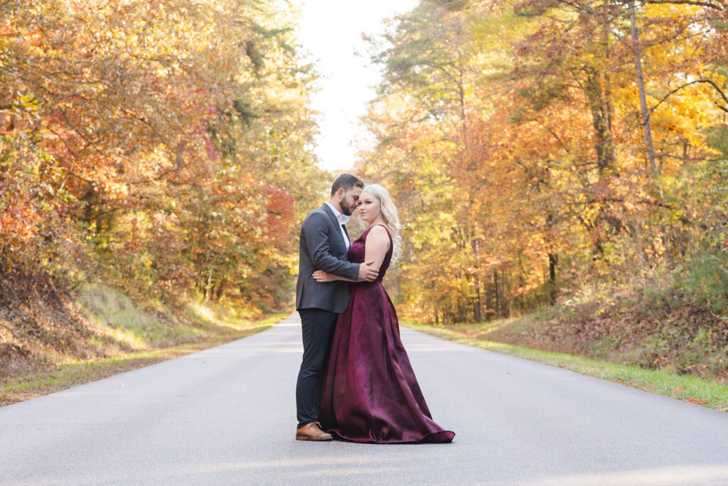 wide angle of Newly engaged couple standing on blue ridge parkway in formal attire with colorful fall trees