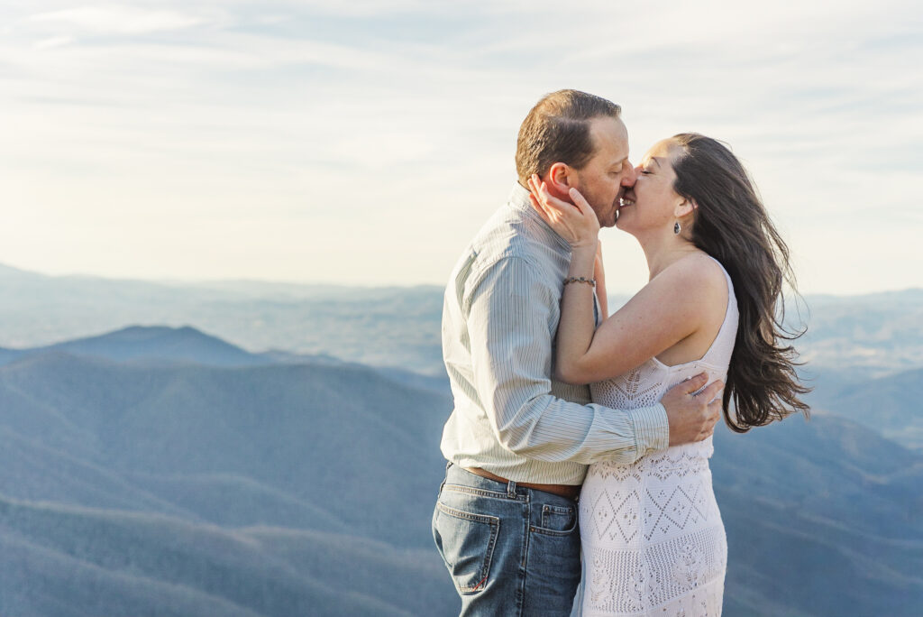 Couple embracing at the top of Craggy Pinnacle.with the blue ridge mountains in the background