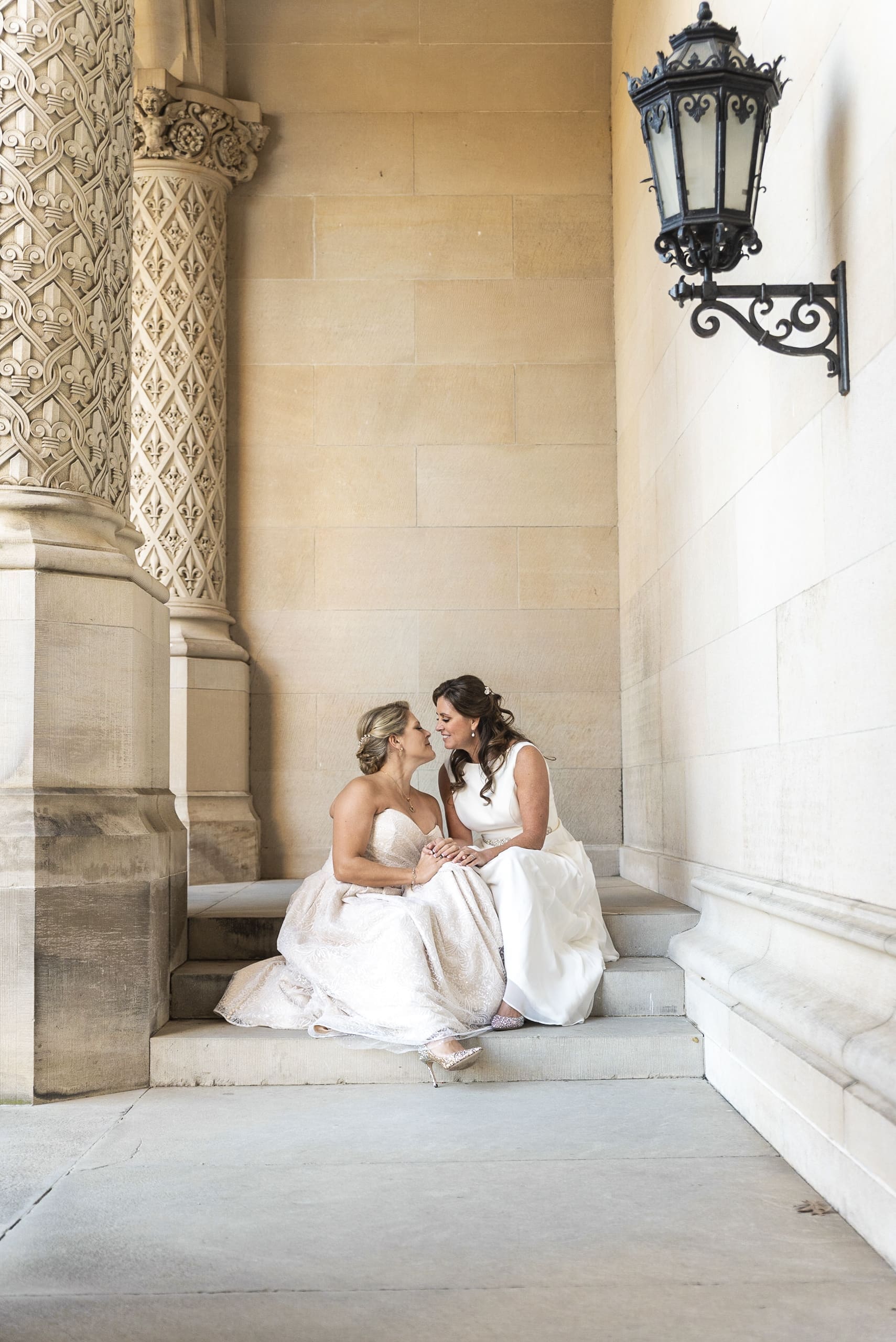 wide image of brides sitting next to each other surrounded by the architecture of the biltmore estate