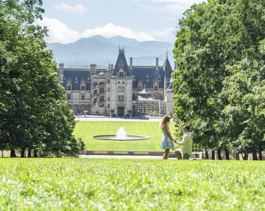 Biltmore estate proposal, man on one knee proposing to his girlfriend at the top of Diana Lawn with the estate and blue ridge mountains in the background