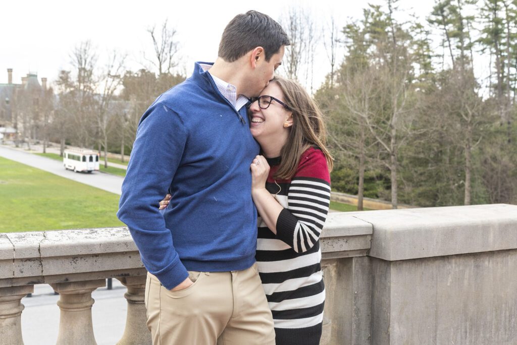 couple hugging after proposal. he is kissing her forehead and she has a big smile