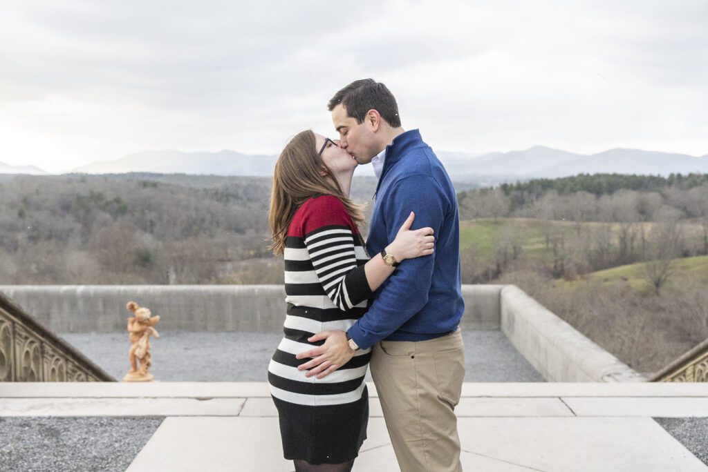 newly engaged couple standing and kissing on south terrace at Biltmore estate with blue ridge mountains in background