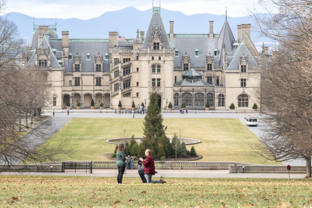 Biltmore estate proposal, man on one knee proposing to his girlfriend at the top of Diana Lawn with the estate in the background during christmas