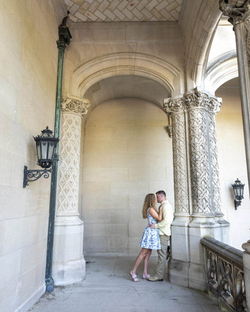 newly engaged couple, man is leaning with his back on a pillar with woman leaning into him and couple is kissing surounded by Biltmore Estate Architecture