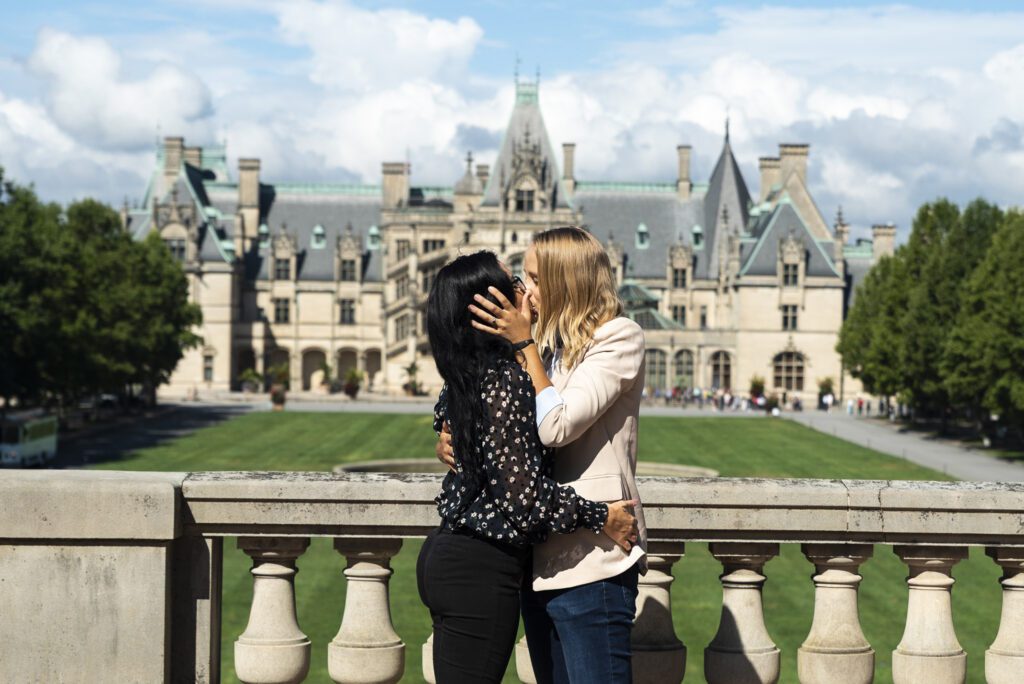 Biltmore estate proposal, lesbian couple, couple standing on the esplanade kissing after proposal with the estate in the background on a sunny day