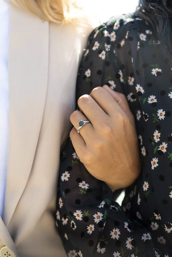 close up of engagement ring on finger with hand around partners arm