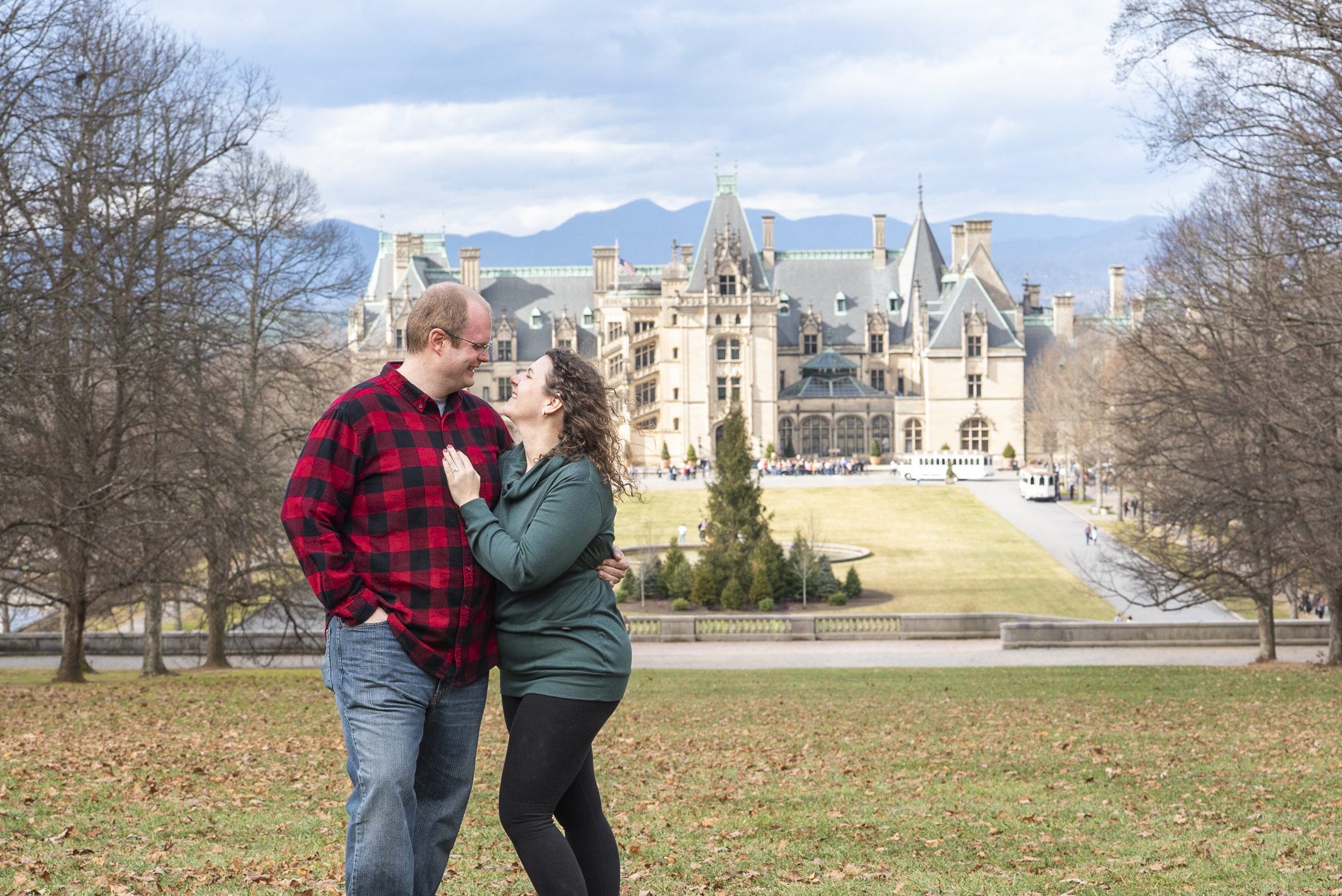 couple standing on high lawn at Biltmore Estate hugging immediately after proposing with Biltmore Estate in the background