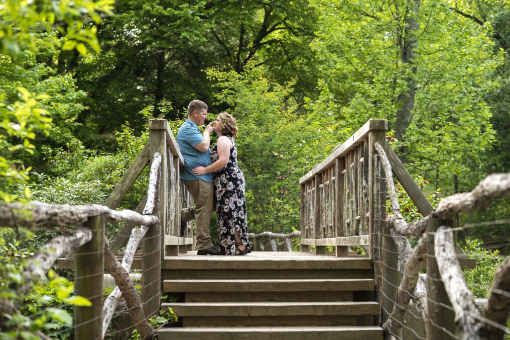 couple standing on bridge in Biltmore estate bass pond kissing