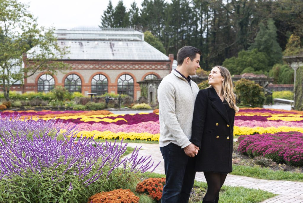 newly engaged couple standing in biltmore flower Garden looking at each other with colorful fall flowers around