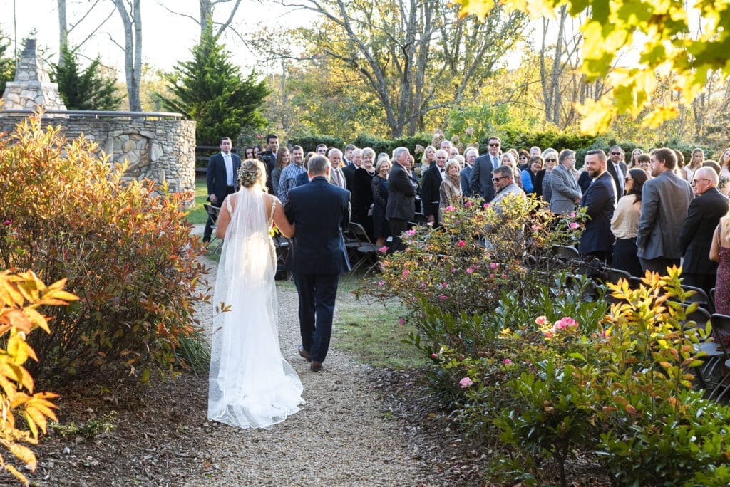 father walks bride down the aisle as he gives her away during outdoor wedding ceremony with mountains in background at Crest center and pavilion