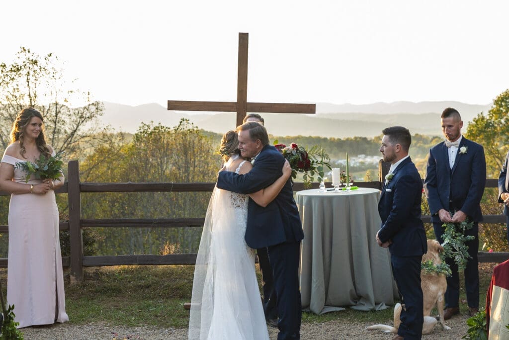 bride and father hug as he gives her away during outdoor wedding ceremony with mountains in background at Crest center and pavilion