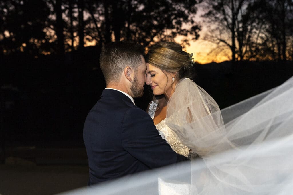 bride and groom forehead to forehead with sunset in background and bridal veil trailing in foreground at crest center and pavilion asheville