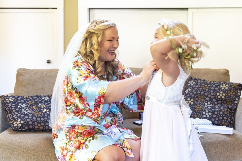bride putting necklace on flower girl daughter