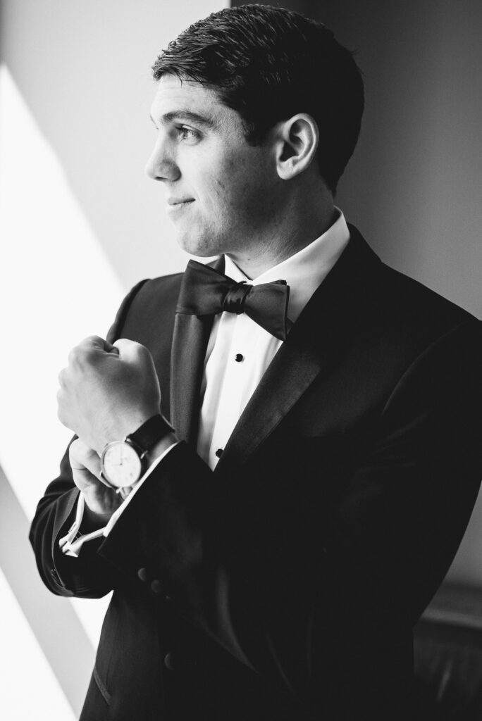 groom portrait with him looking out window pose showcasing watch.