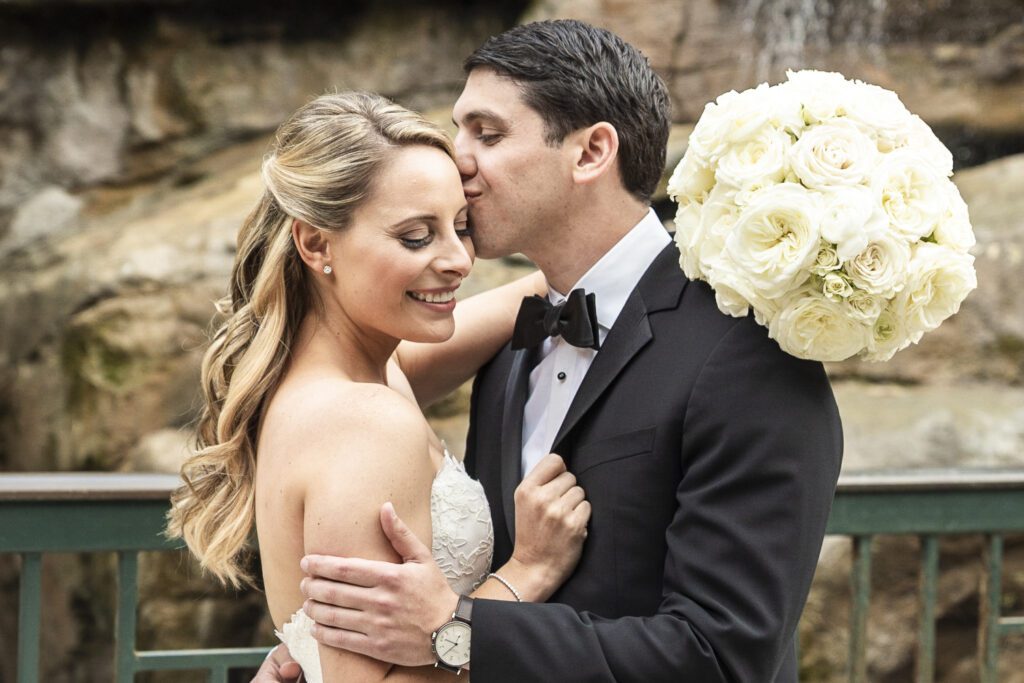 groom kisses bride's forehead with waterfall in background at Grove Park Inn