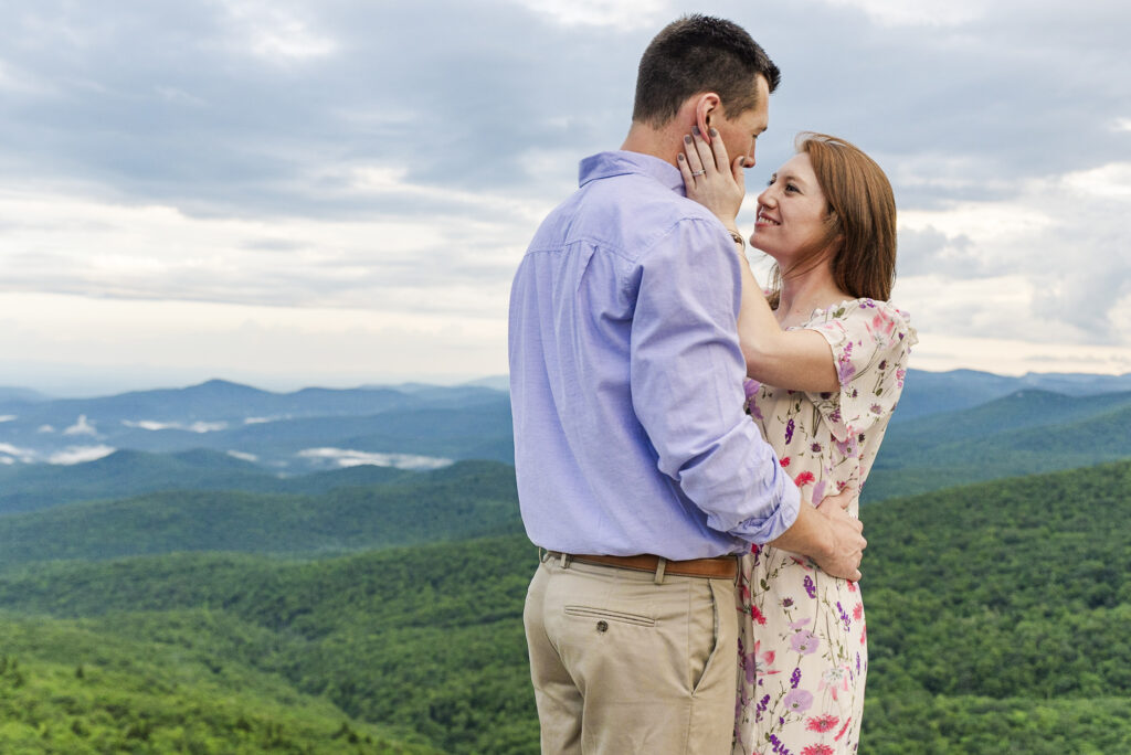 couple embracing at the top of Linville falls on a cloudy spring day with a long view of the blue ridge parkway in the background 