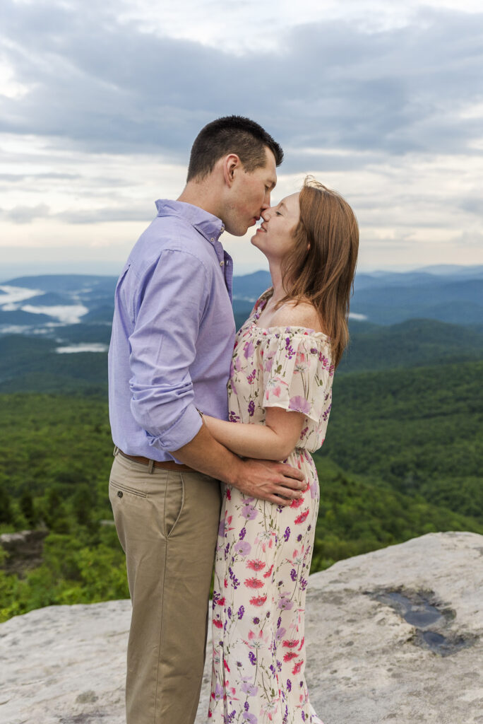 couple embracing at the top of Linville falls on a cloudy spring day with a long view of the blue ridge parkway in the background
