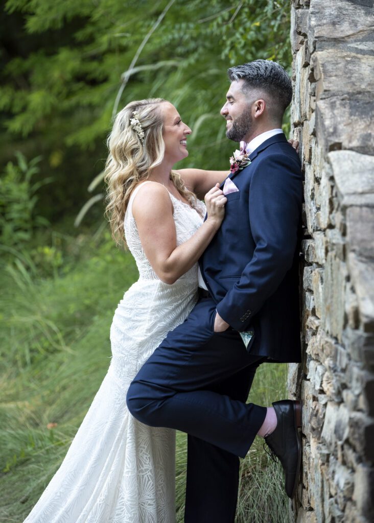 groom leaning on stone wall, bride leaning into groom at NC Arboretum