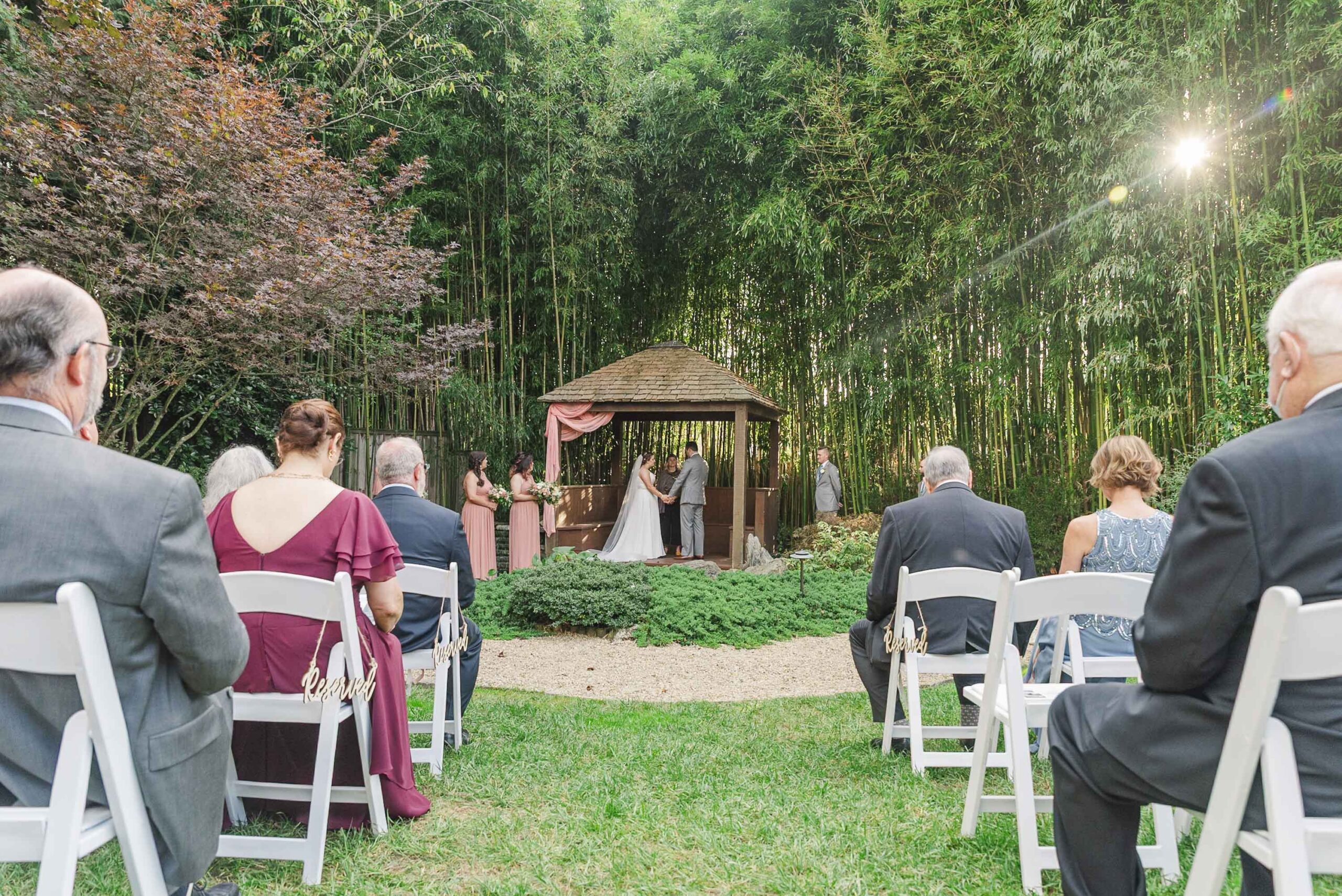 wide image of bride and groom during ceremony surrounded by bamboo, landscaping, and seated guests at Weaver House wedding venue