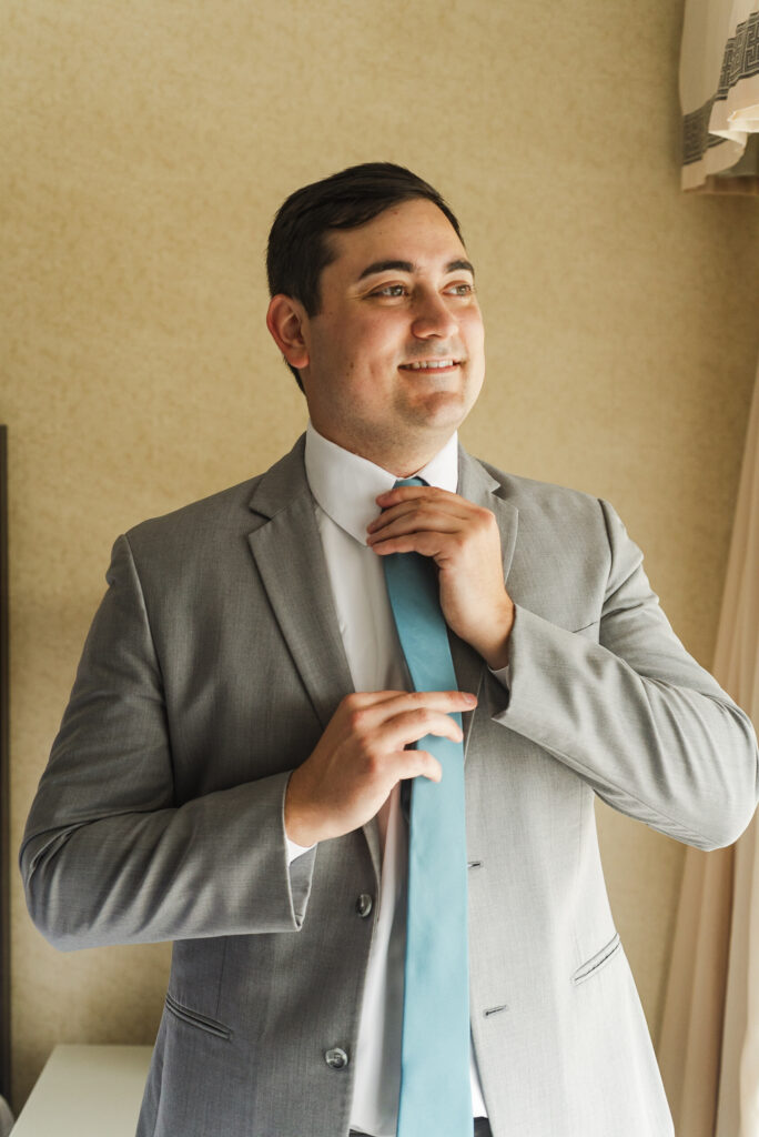 three quarter portrait of groom adjusting his tie
